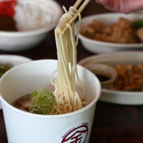 A person using chopsticks to lift noodles from a white bowl, with various dishes in the background.