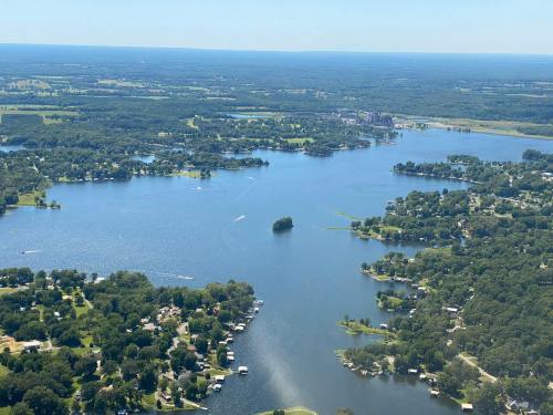 Aerial view of a large lake surrounded by greenery and small residential areas on a sunny day.