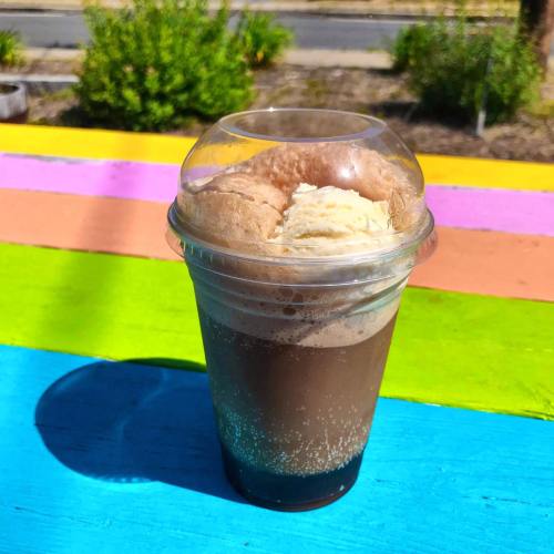 A clear cup filled with a chocolate drink topped with ice cream, placed on a colorful wooden surface.
