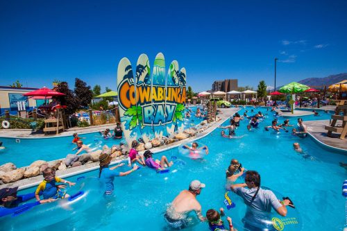 A vibrant water park scene with families enjoying a lazy river, colorful umbrellas, and a sign for Cowabunga Bay.