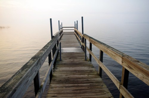 A wooden dock extends over calm water, surrounded by a misty atmosphere.