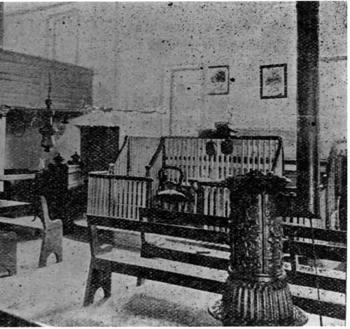 Interior of a historic room with wooden benches, a partition, and decorative lamps.