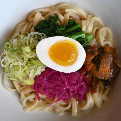 A bowl of noodles topped with greens, pickled cabbage, mushrooms, and a soft-boiled egg with a runny yolk.