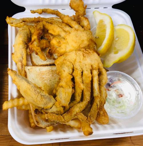 A takeout container with fried crab, toast, lemon wedges, and a side of coleslaw.