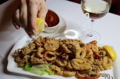 A plate of fried calamari with lemon and marinara sauce, accompanied by a glass of white wine.