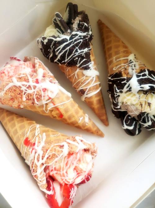 Four ice cream cones in a box, topped with various flavors and drizzled with white sauce.