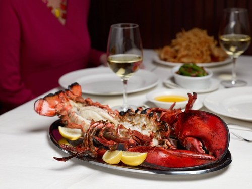 A beautifully presented lobster on a platter, garnished with lemon slices, alongside glasses of white wine.