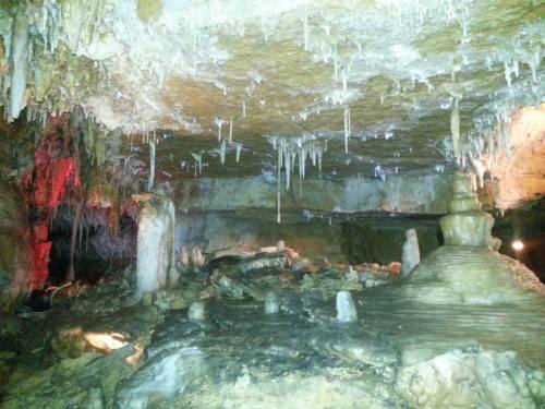 Stalactites and stalagmites in a dimly lit cave, with colorful lighting highlighting the rock formations.
