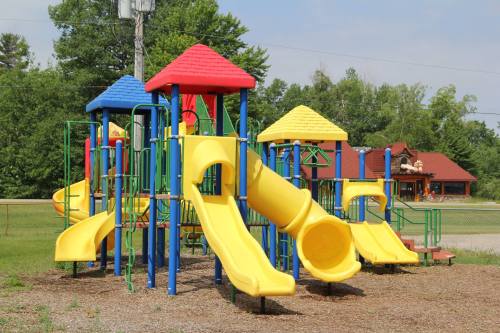 Colorful playground equipment with yellow slides and red and blue roofs, set in a grassy area with trees in the background.