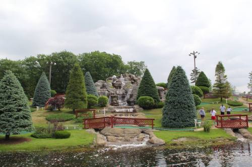 A scenic mini-golf course featuring a waterfall, lush greenery, and visitors enjoying the outdoor space.