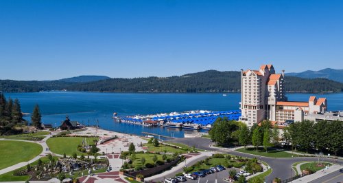 A scenic view of a marina with blue boats, a hotel, and lush greenery under a clear blue sky.