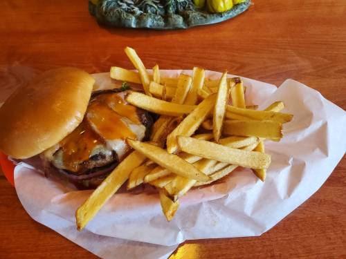 A cheeseburger with melted cheese and lettuce, served with a side of golden French fries on a paper-lined plate.