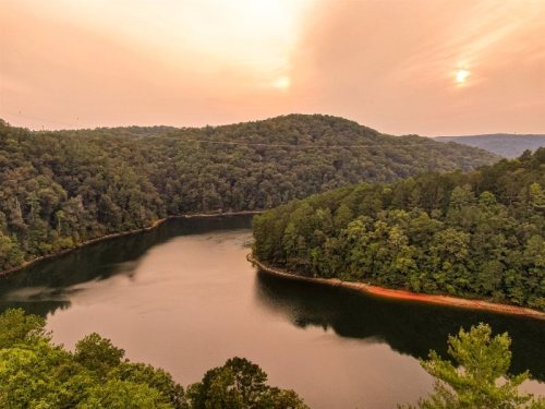 A serene lake surrounded by lush green hills under a hazy sunset sky.