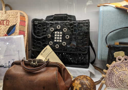 A vintage black handbag designed to resemble a rotary phone, displayed among other bags and items.