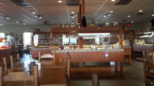 Interior of a restaurant featuring buffet tables, wooden chairs, and a spacious dining area with natural light.
