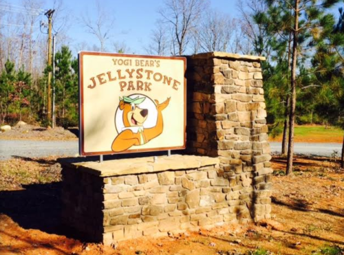 Sign for Yogi Bear's Jellystone Park, featuring a cartoon bear and surrounded by trees and a stone structure.
