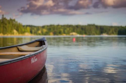 A red canoe floats on calm water, with trees and a cloudy sky reflected in the serene lake.