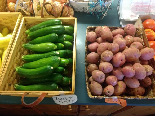 Two baskets of fresh produce: one with green zucchinis and the other with red potatoes, both labeled with prices.