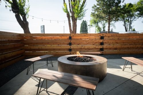 A cozy outdoor fire pit surrounded by wooden benches and a fenced area, with trees in the background.