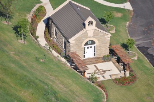 Aerial view of a small stone building with a metal roof, surrounded by landscaped gardens and pathways.