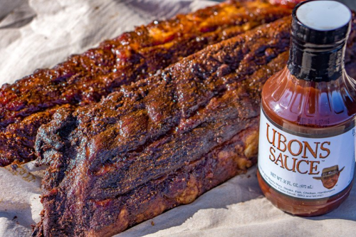 Two racks of smoked ribs with a bottle of Ubon's sauce on a brown paper surface.