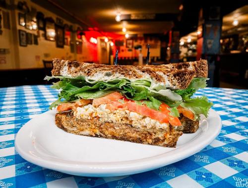 A hearty sandwich with layers of lettuce, tomato, and a savory filling, served on a plate in a cozy restaurant setting.