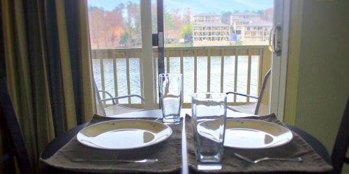 A dining table set for two, overlooking a serene lake view through sliding glass doors.