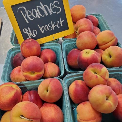 Baskets of fresh peaches with a sign reading "$10 basket" displayed at a market.