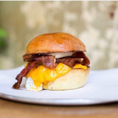A delicious burger with bacon, melted cheese, and a fried egg on a soft bun, served on a white plate.