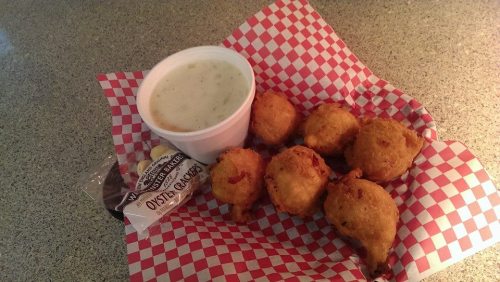 A plate of golden fried fritters with a cup of creamy soup, served on a checkered paper.