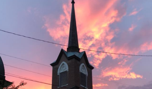 A church steeple silhouetted against a vibrant pink and orange sunset sky.