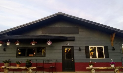 A gray and red building with flower pots, a closed sign, and a welcoming entrance under a pastel sky.