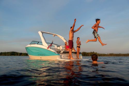 A family enjoys a summer day on a boat, with kids jumping into the water and adults watching happily.