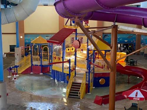 Colorful indoor water play area with slides, water features, and a splash zone.