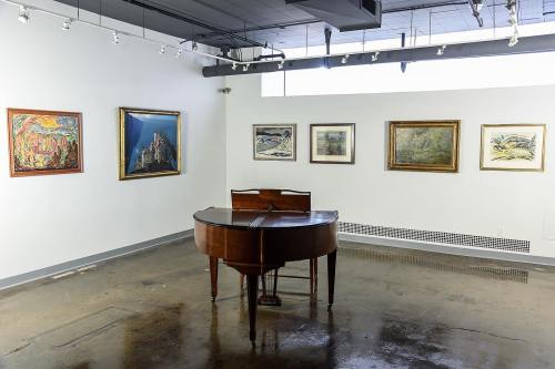 A wooden piano in a gallery surrounded by various framed paintings on the walls.