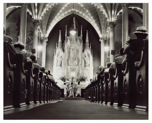 A black-and-white photo of a church interior, featuring a decorated altar and pews filled with worshippers.