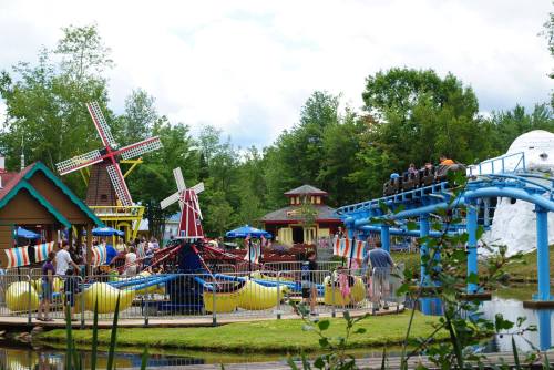 A colorful amusement park scene with rides, a windmill, and people enjoying the attractions near a pond.