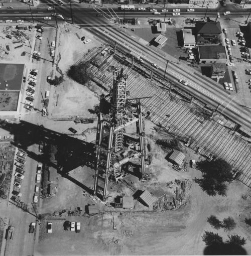 Aerial view of a construction site with a large drilling rig and surrounding roads, vehicles, and buildings.
