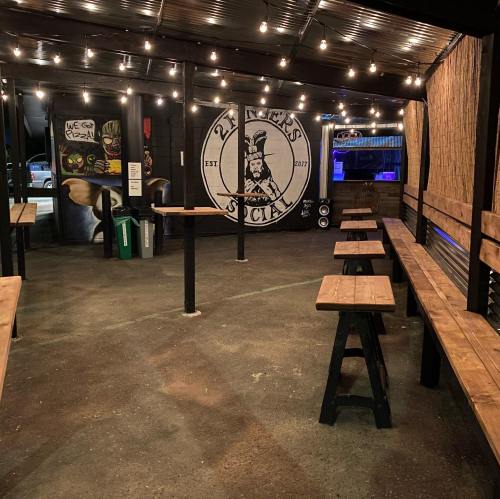 Outdoor seating area with wooden benches, string lights, and a mural of a logo on the wall.