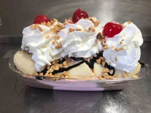 A banana split topped with whipped cream, chopped nuts, chocolate syrup, and cherries.