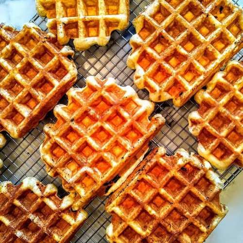 A close-up of golden-brown waffles arranged on a cooling rack, showcasing their crispy texture and grid pattern.