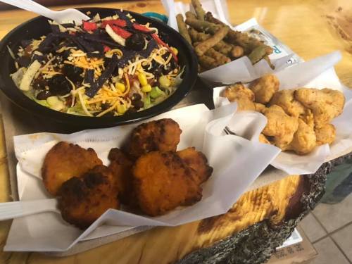 A colorful salad with black beans, cheese, and tortilla strips, alongside fried snacks and green beans on a wooden table.