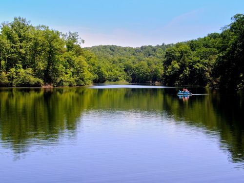 A serene lake surrounded by lush green trees, with two people kayaking on the calm water under a clear blue sky.