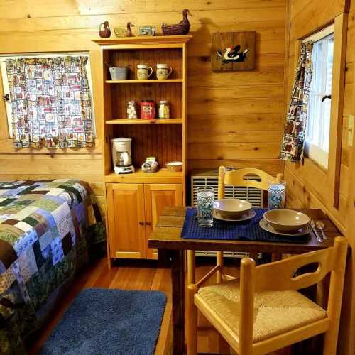 Cozy cabin interior with a quilted bed, wooden furniture, and a dining table set for two.