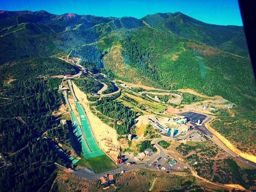 Aerial view of a mountainous landscape featuring a ski jump, roads, and a facility surrounded by greenery.