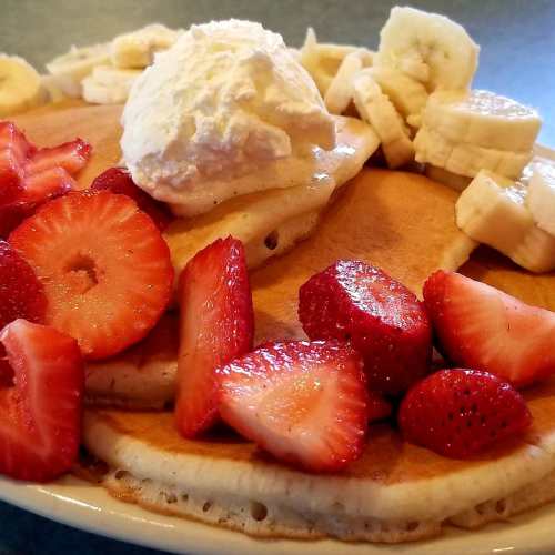 A stack of pancakes topped with whipped cream, sliced bananas, and fresh strawberries.