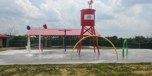 Colorful water play area with a red water tower, spray features, and a concrete surface under a cloudy sky.