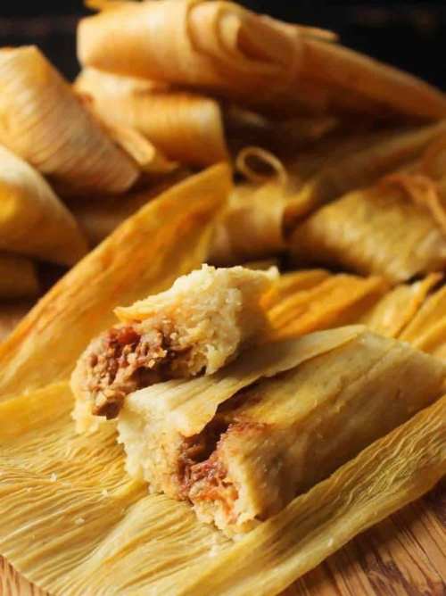 A close-up of a tamale cut in half, revealing its filling, with more tamales in the background.