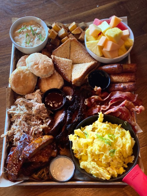 A large platter of assorted breakfast foods, including biscuits, bacon, eggs, fruit, and various meats.