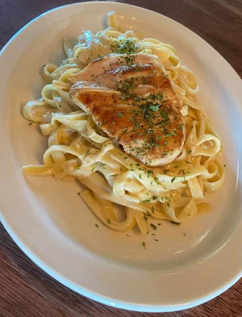A plate of fettuccine pasta topped with grilled chicken and garnished with herbs.